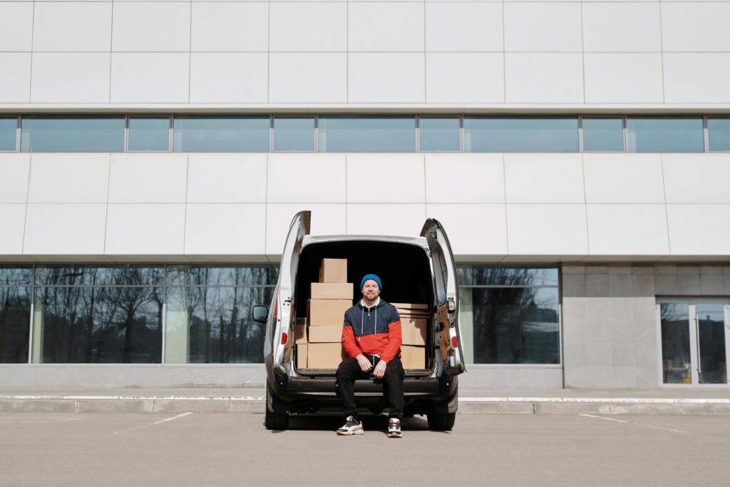 pexels-photo-4391639-4391639 Man in a colorful jacket sitting by a van with boxes in an urban setting.