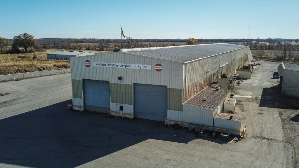 pexels-photo-8100831-8100831 Aerial view of a large industrial warehouse in Madisonville, KY, USA, under clear blue skies.